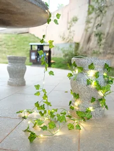 Detailaufnahme von leuchtenden LED-Efeu-Lichterketten auf einem Steingartensockel.