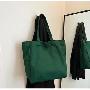 Close-up view of a green canvas tote bag hanging in a minimalist interior setting.