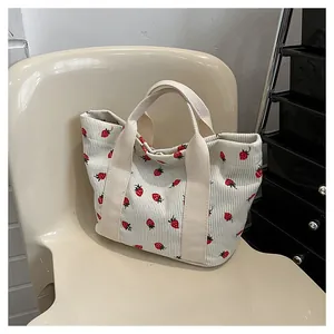 Detailed view of a white corduroy tote bag featuring cute red strawberry prints