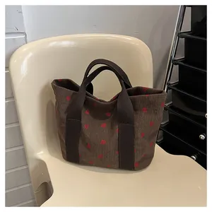 Corduroy tote bag with cute red strawberry print on a brown base, shown in lifestyle scene.