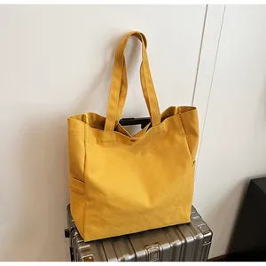 Detailed view of a large yellow canvas tote bag placed on a silver metallic suitcase