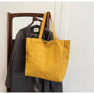 Minimalist yellow canvas tote bag hanging over a grey blazer in a lifestyle setting