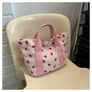 Close-up of a pink corduroy tote bag with cute strawberry prints on a beige chair