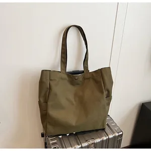 Olive green canvas tote bag with side pockets resting on a silver suitcase detail view