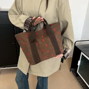 Brown corduroy tote bag with strawberry print being held by a model in casual wear