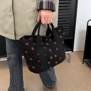 Versatile casual black corduroy tote bag featuring pink strawberry prints held by model