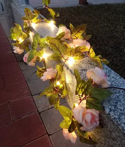 Detailansicht von rosa Rosen-Lichterkette mit warmweißen LEDs an einer Steinmauer