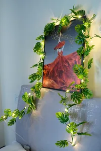 Dekorative warme LED-Lichterkette mit künstlichen grünen Monstera-Blättern an der Wand