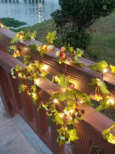 Warme LED-Deko-Rebenlichter mit Seidenrosen am hölzernen Gartenzaun bei der Abenddämmerung.