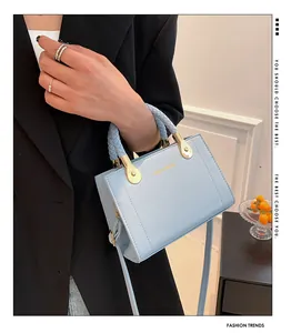 Detail shot of an elegant light blue woven handbag held by a model in a black blazer.