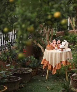Detail view of a rustic cream and orange pleated ruffle edge tablecloth in a garden