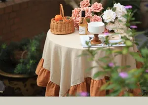 Detailed view of a round beige tablecloth with orange ruffles in a garden setting.