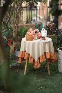 Outdoor garden setting featuring a two-tone ruffled round tablecloth in beige and orange
