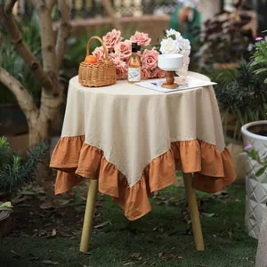 Detailed view of a modern round tablecloth with orange ruffled edges in a garden setting