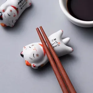 Repose-baguettes mignon Maneki-neko en céramique avec baguettes en bois sur fond gris.