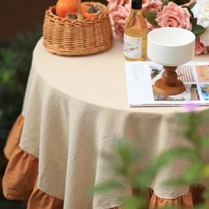 Close-up of the elegant beige tablecloth featuring a ruffled orange hem on a round table