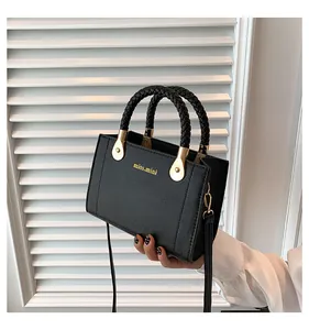 Detailed view of a black luxury handbag featuring braided top handles and gold hardware.