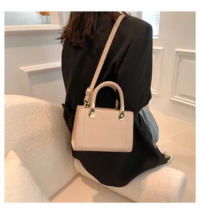 Side view of a model carrying a beige structured handbag with elegant woven handles.