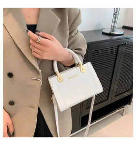 Close-up of white pebbled leather handbag with gold miss.mini logo and woven handle
