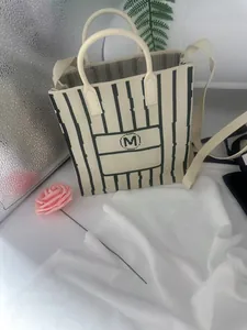 Close-up detail of a stylish knitted cream tote bag featuring black stripes and (M) logo
