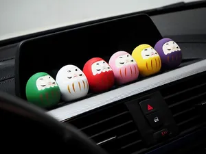 Sechs bunte Daruma-Glücksbringer auf dem Armaturenbrett eines Autos als Innendekoration