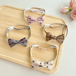 Four floral cat bowtie collars in pink, brown, purple and beige on a wooden tray