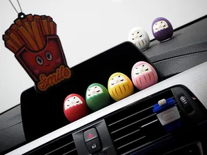 Detailansicht von bunten Mini-Daruma Auto-Zierelementen auf einem schwarzen Armaturenbrett.