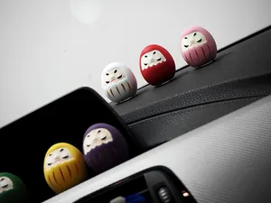 Set bunter Mini-Daruma-Puppen als Dekoration auf einem modernen Auto-Armaturenbrett