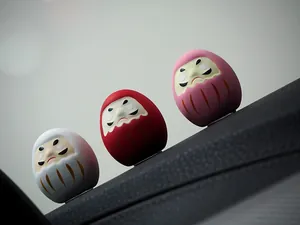 Nahaufnahme von drei farbenfrohen japanischen Mini-Daruma-Puppen auf einem Armaturenbrett