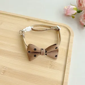 Close-up detail of brown floral pet bow tie collar with white buckle on wooden tray