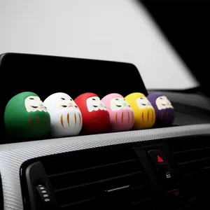 Detailansicht bunter japanischer Daruma-Puppen auf einem modernen Auto-Armaturenbrett.