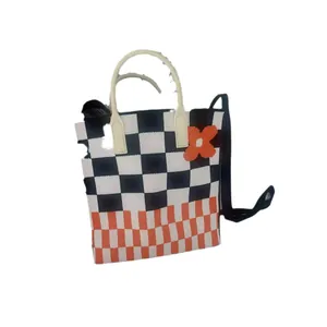 Knitted checkerboard crossbody bag featuring orange flower detail and white top handles