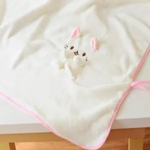 Détail d'une couverture en flanelle blanche avec tête de chat en peluche et bord rose.