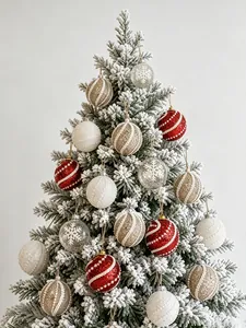 Nahaufnahme von rot-weiß-goldenen Ornamenten mit Schneeflocken auf einem beschneiten Weihnachtsbaum.