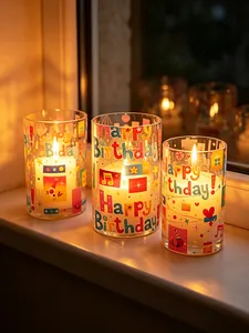 Close-up of birthday-themed LED candles with 'Happy Birthday' glass holders on sill