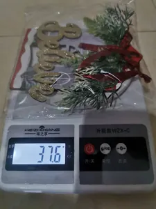 Macro detail of a wooden Believe Christmas ornament with red ribbon weighing 37.6g on a scale.