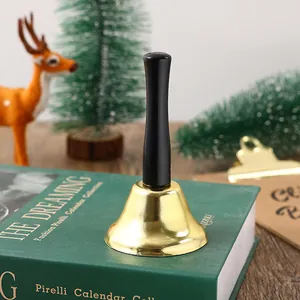 Macro view of a classic gold Christmas handbell with a black handle on a decorative book