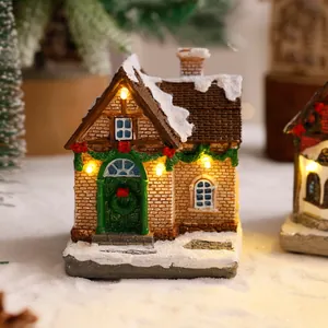 Primo piano di casa di Natale in resina illuminata con tetto innevato e ghirlanda festiva.
