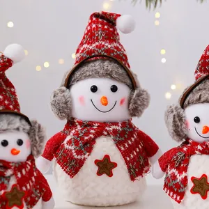 Primer plano de un lindo muñeco de nieve de peluche con gorro y bufanda de punto rojos.
