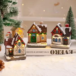 Dettaglio di tre casette di Natale in miniatura in resina illuminate su un fondo nevoso bianco