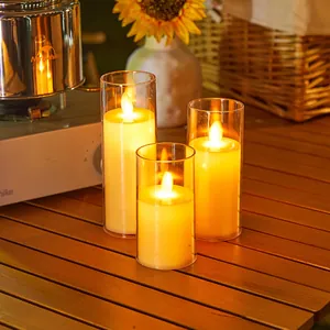 Set of three decorative LED flameless candles in glass cylinders on a warm wooden table.