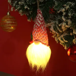 Vue détaillée d'un gnome de Noël lumineux suspendu à une branche de sapin enneigée festive