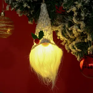 Gros plan d'un gnome de Noël lumineux suspendu à une branche de sapin enneigée.