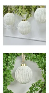 Detailed close-up of white knitted Christmas ball ornaments on green fir tree branches