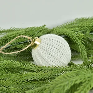 Elegant white knitted Christmas ball ornament with gold cap on green pine needles