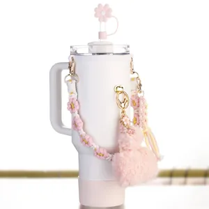 Vista detallada de un vaso blanco con tapa de pajita de flor rosa y llavero de corazón suave
