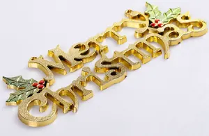 Detailed view of golden Merry Christmas hanging plaque with green holly leaves decoration.