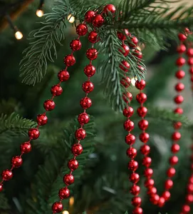 Primer plano de una guirnalda de cuentas rojas navideñas sobre ramas de pino verde.
