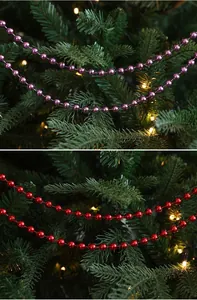 Vista detallada de cadenas de perlas festivas rojas y rosas en un árbol de Navidad iluminado