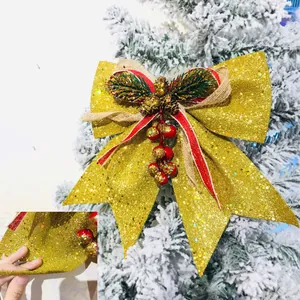 Dettaglio fiocco di Natale glitter oro con pigne e bacche su un albero innevato